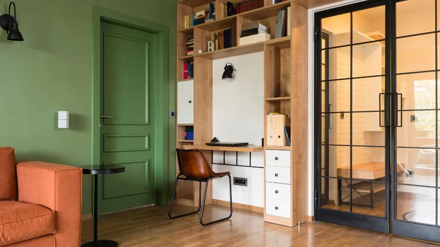 A cozy home office with green walls, a wooden desk, and bookshelves.