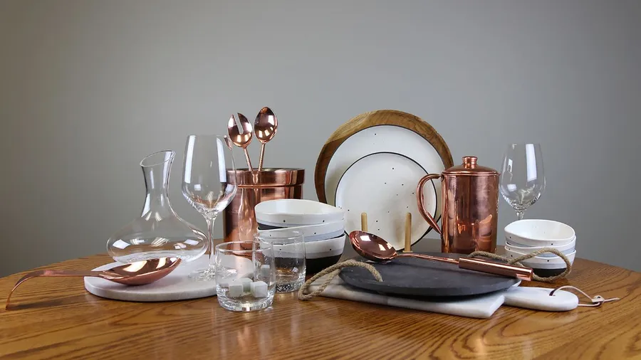 Table setting with rose gold cutlery, flowers, and lace fabric.