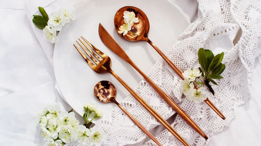 Stylish dining area with copper-colored cutlery, flowers, and lace fabric.