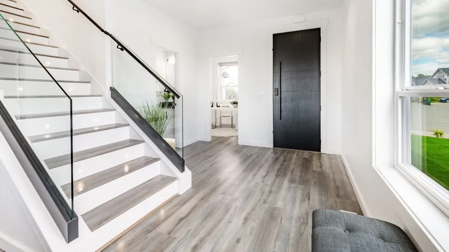 A minimalist entrance hall with a black door, stylish staircase, and a hard word flooring.