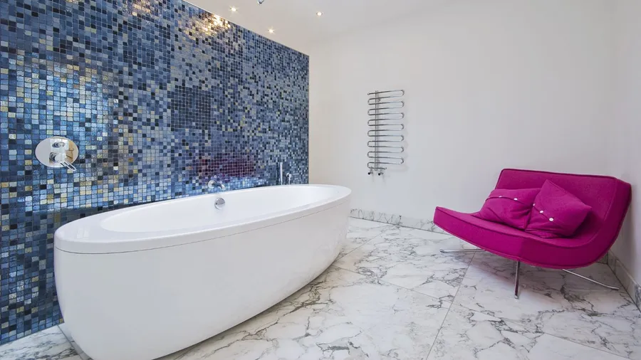 A contemporary bathroom with a colorful mosaic wall, a sleek white tub, and a pink sofa with cushions.