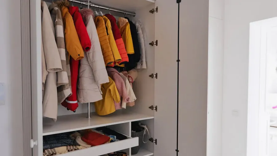 A wardrobe with colorful winter coats neatly arranged on hangers and storage baskets below.