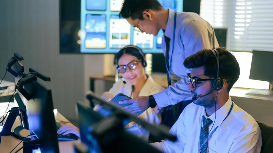 Professional diverse team in headsets collaborates in a control center. Monitoring live data on screens and tablets for international flight. Network security, and corporate operation application