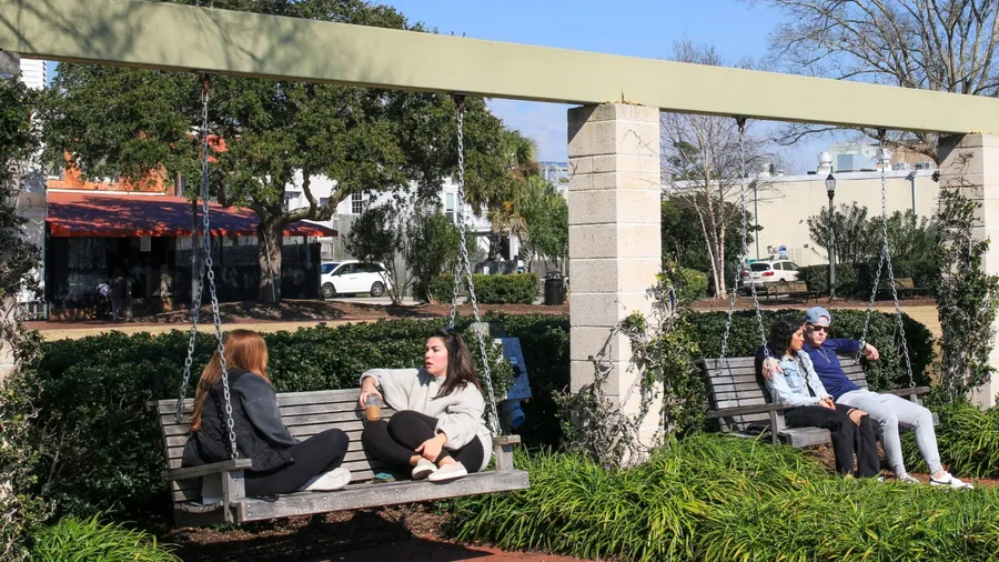 Beaufort, South Carolina, USA - 19 of February 2024: A couple of people relaxing on wood bench swings in Henry Chambers Park Beaufort South Carolina.