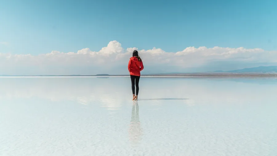 Woman tourist & beautiful mirror reflection on blue sky and cloud on Bolivia's Salt Flats. Shot in Salar de Uyuni salt flat. Water reflection of clouds and empty space. Holiday, vacation travel scene