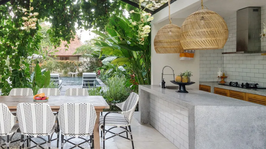 An inviting outdoor kitchen includes a spacious dining table, stylish chairs, and lush greenery, perfect for entertaining in a natural setting.
