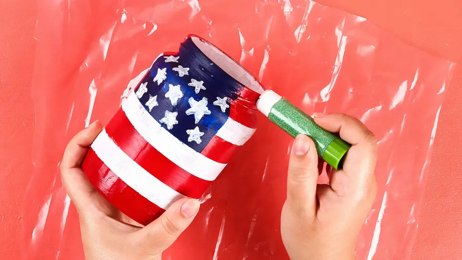 A person painting an American flag on a mason jar for Memorial's Day decor.