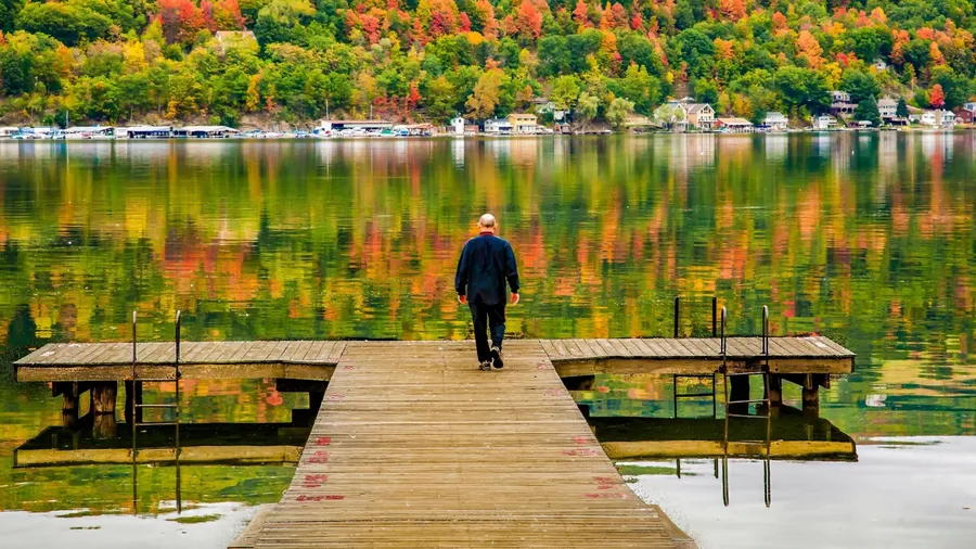 Seneca Lake in the Finger Lakes Region of Upper New York. Autumn color reflected in the lake. Man walking on swimming and fishing dock