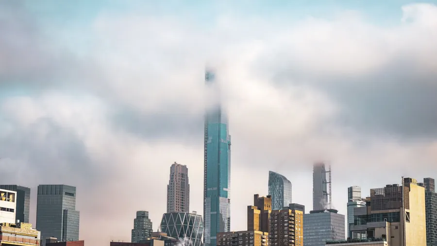 Fog partially shrouds the New York City skyline, with tall skyscrapers peeking through misty clouds. This atmospheric shot captures the city in a serene, mysterious mood.