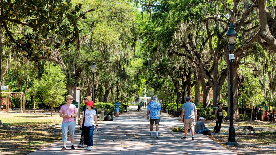 Savannah, USA - May 11, 2018: Famous water fountain in Forsyth park in Georgia during sunny day in summer with people tourists walking on alley street