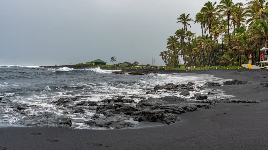 Punaluʻu Beach, Hawaii USA 11 21 2022: Punaluʻu Beach on a gloomy day with tourist enjoying the black sand and lifeguards watching over the ocean