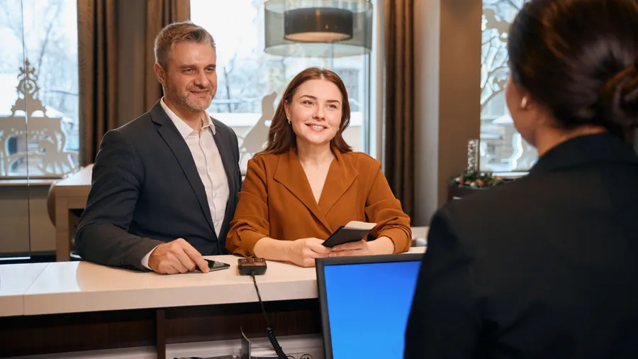 European couple looking at female reception desk during check-in in hotel lobby