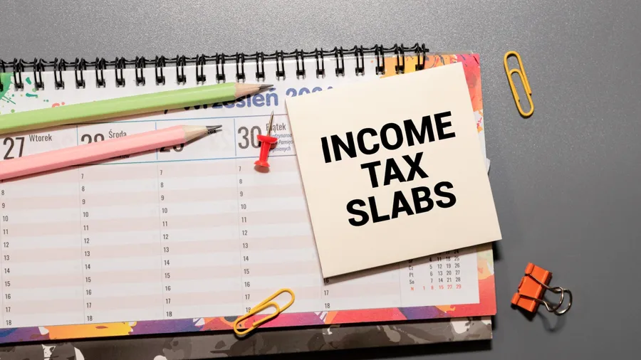 Income Tax Slabs inscription on white card. Workplace background, top view.