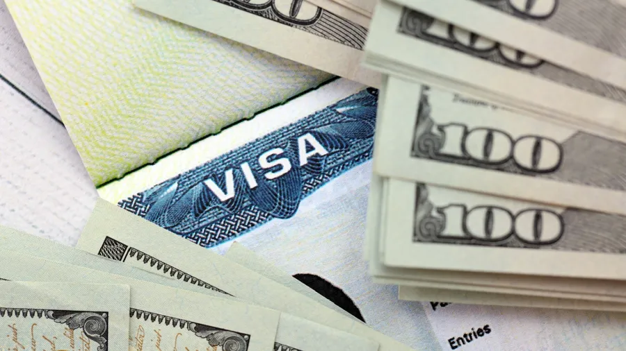 US visa sticker seen in passport and dollar banknotes placed on top. Concept for immigration and visa fees