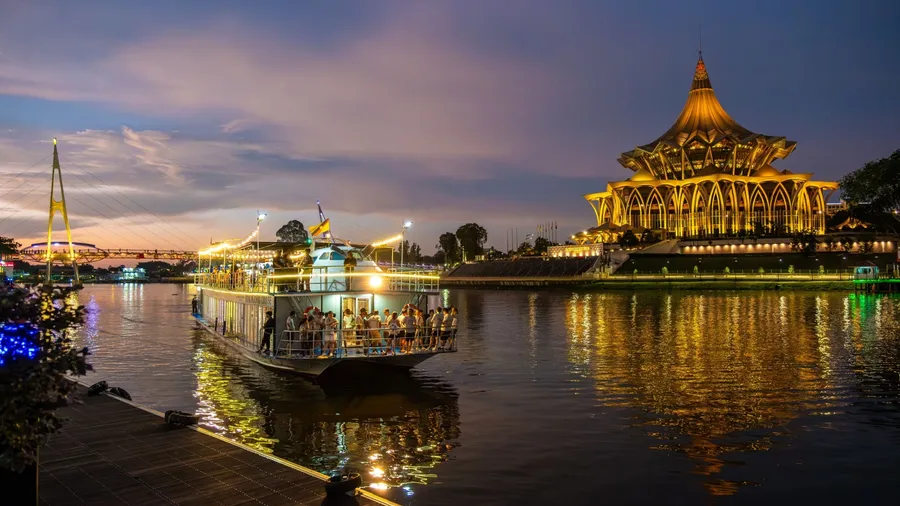 SARAWAK, MALAYSIA - SEPTEMBER 16, 2023: Sarawak River Cruise boat with a background of State Legislative Assembly building during a sunset cruise. One of the popular tourist attractions in Kuching.