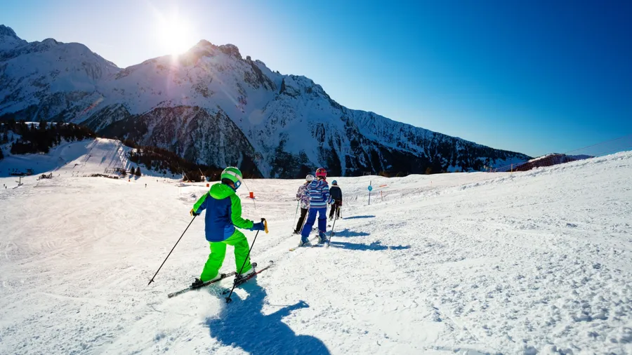 Group of children ski on the hill together on Alpine resort over mountains on background