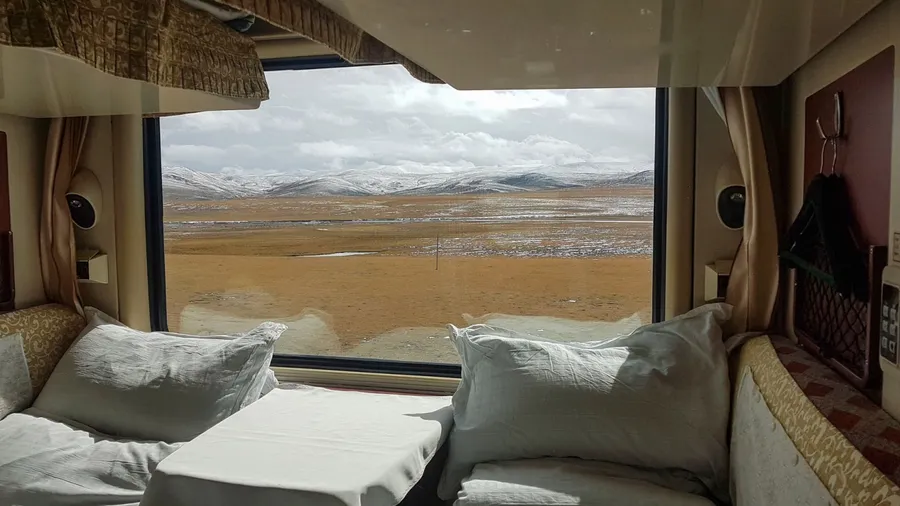 CLOSE UP: Picturesque view of the snowy Tibetan landscape from a comfortable sleeper train. Two beds in a luxury cabin lay empty as the Trans-Himalayan overnight train crosses the Chinese countryside.