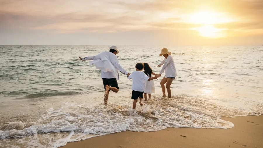 Happy Asian parents and daughters have delightful time on beach. Little girls bond with their mother and father running jumping and pretending to fly with arms wide open. Family fun under sun.
