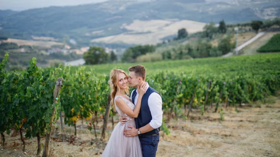 young beautiful wedding couple walking at sunset in Tuscany in Italy near the vineyards bride in beautiful dress groom stylishly dressed