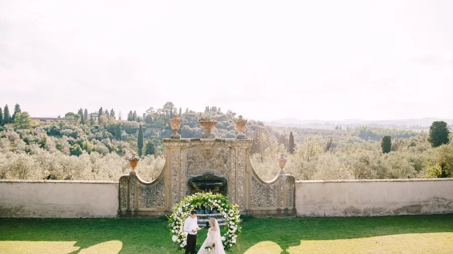Florence, Italy - 02 october 2019: Wedding at an old winery villa in Tuscany, Italy. Wedding couple under a round arch of flowers. The groom reads wedding vows.