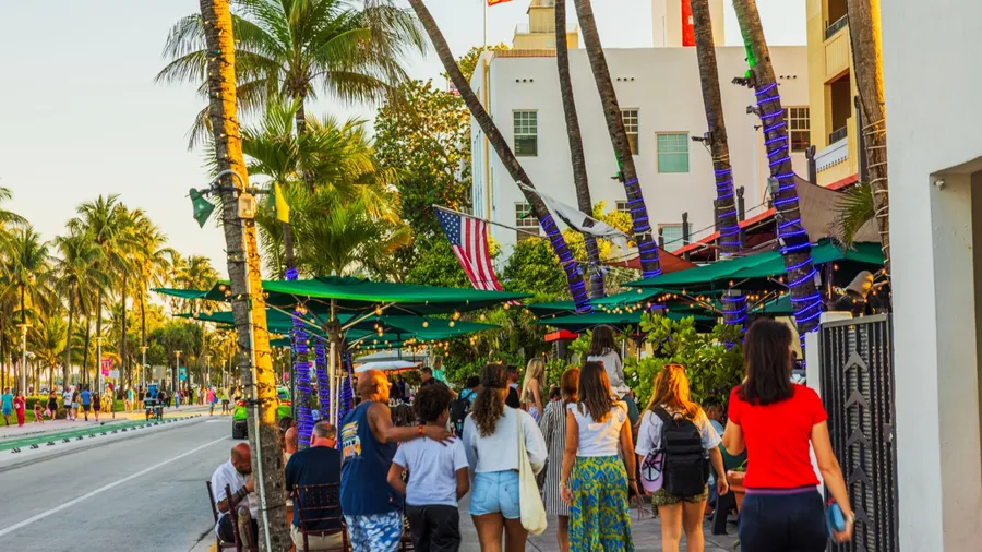 Evening view of Ocean Drive in Miami Beach with tourists walking by outdoor restaurants and illuminated palm trees. Miami Beach. USA. 10.26.2025.