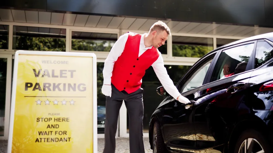 Personalized Luxury Valet Service: A Young Businessman Receives Receipt from Uniformed Attendant in Modern City Setting. Professionalism and Satisfaction Guaranteed.
