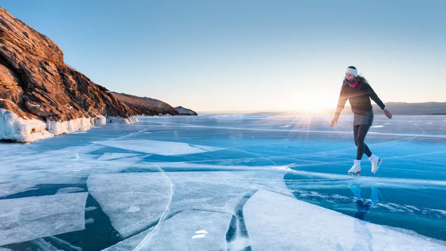 A young happy woman is skating on the transparent ice of the frozen Lake Baikal on a sunny winter day - World-famous figure skater "Polina Korobeynikova" performs on Lake Baikal