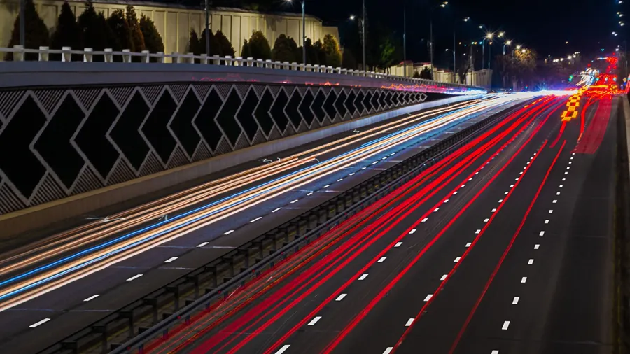 An eight-lane highway at night, illuminated by street lamps. The photo was taken with a long exposure, in which the movement of cars leaves light trails of yellow, blue, red.