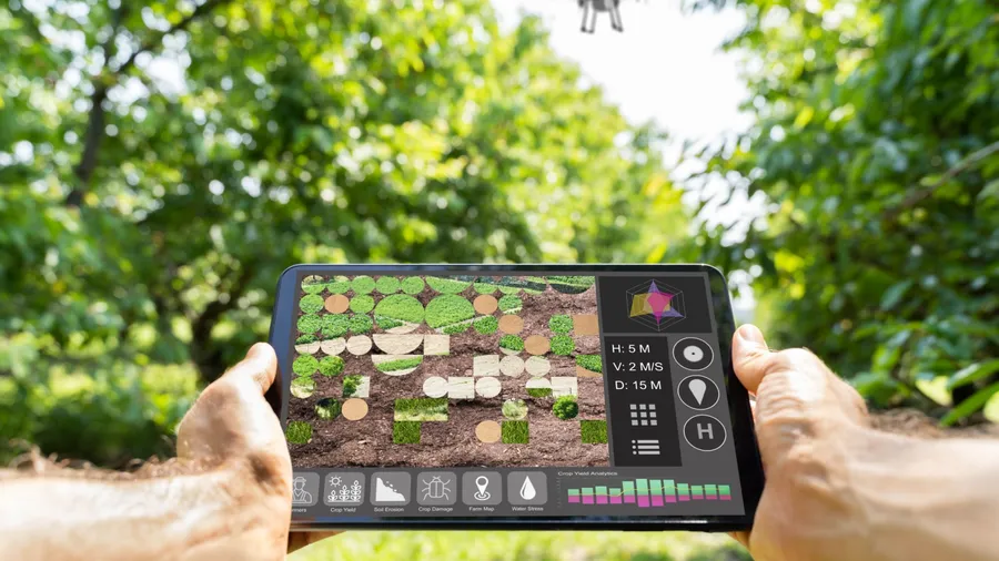 A person holding a tablet displaying a garden layout with a drone in the background.