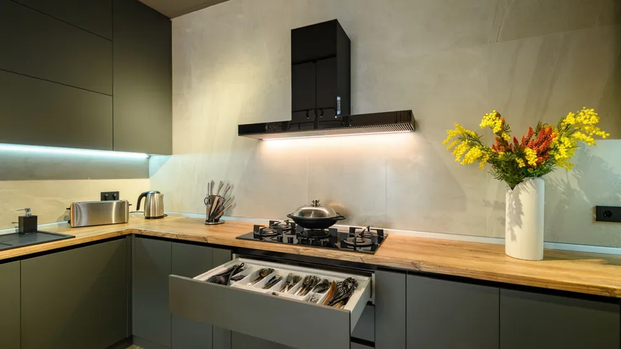 A modern kitchen interior with under cabinet lighting, wooden countertop, and gray cabinets.