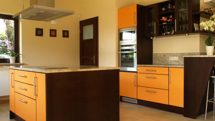 A kitchen interior with orange and brown cabinets, oven, and center island.