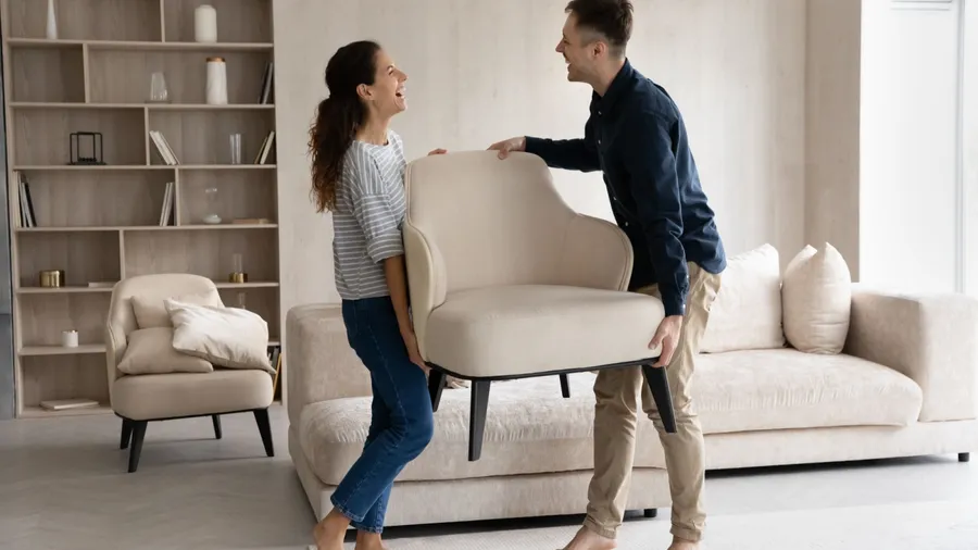 A couple moving an armchair in a living room.