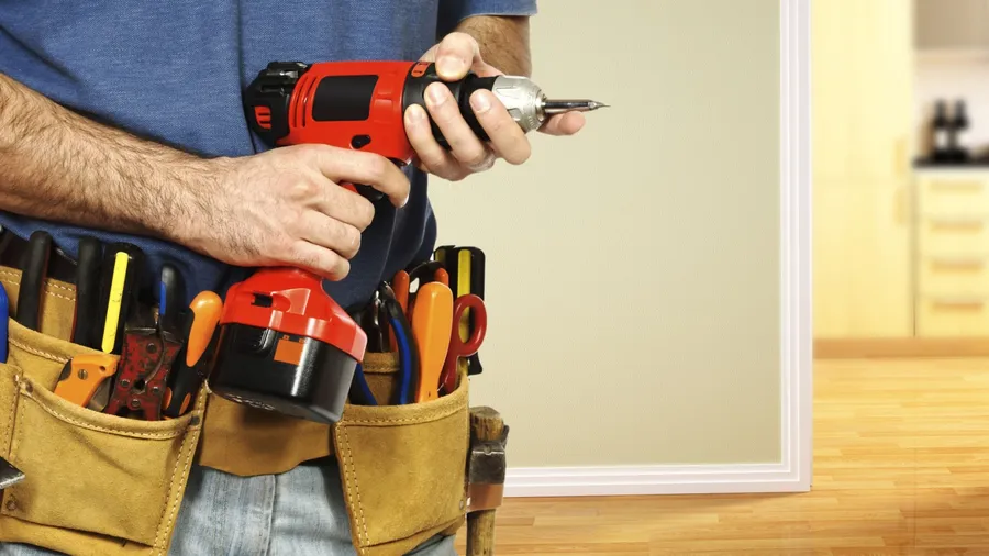 A person holding a red and black cordless drill with a tool belt full of various tools