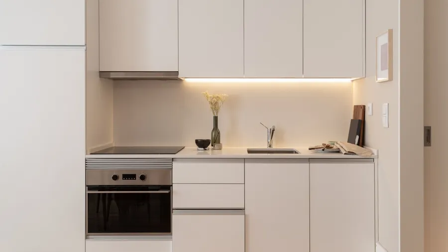 A kitchen interior with warm white cabinets, oven, flower vase, and under-the-cabinet LED light.