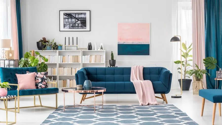 A stylish living room interior with blue sofa, throw pillows, throw blanket, floor lamp, rug, coffee table, bookshelf, and a poster on the wall.