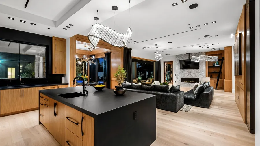 Modern open-plan kitchen and living room with sleek wooden cabinetry, black countertops, and stylish lighting fixtures.