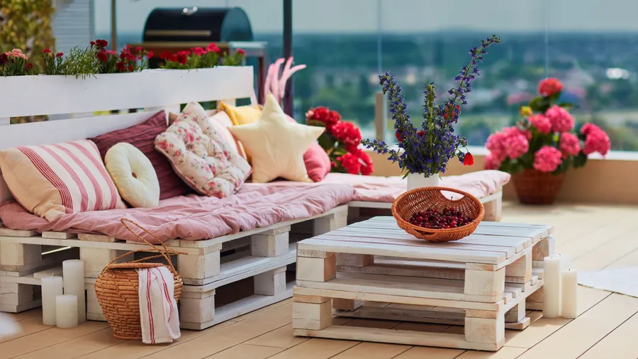 A stylish patio with wooden furniture, cozy throw pillows, plants, and a storage basket on the wooden floor.