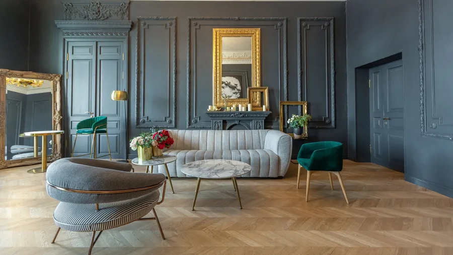 An elegant lounge area featuring a gray striped sofa, green accent chair, and a large gilded mirror reflecting the stylish decor against a dark wall.