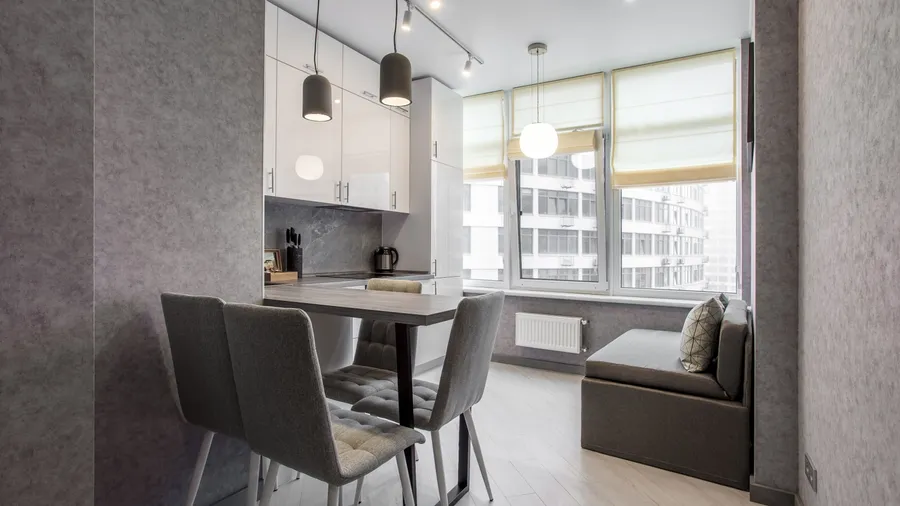 A small, modern kitchen with grey walls, a dining table, and a window seat.