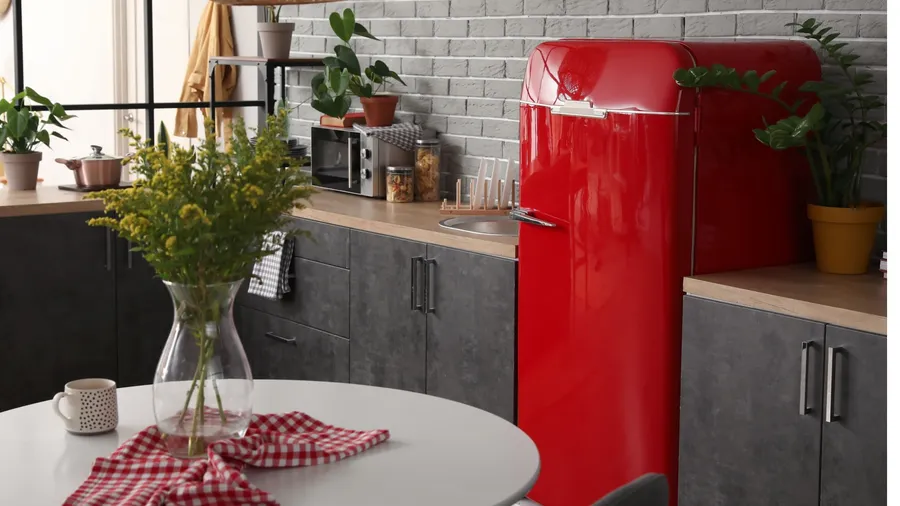 A vibrant red refrigerator stands in a modern kitchen with plants and a round table.