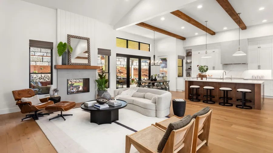 An open concept design house with sofa, rattan chairs, coffee table, and leather recliner, with kitchen and dining space in the background.