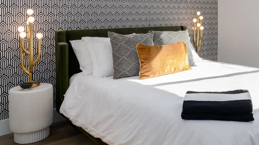 A bedroom interior with a cozy bed, pillows, bedside tables with lamps, and a textured wallpaper on the wall.