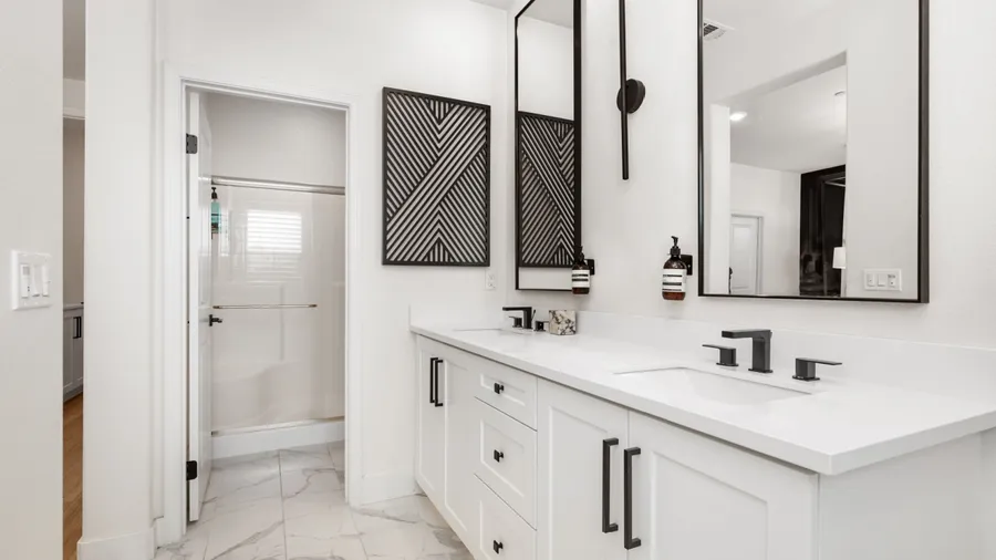 A minimalist white bathroom with black accents and large mirrors.