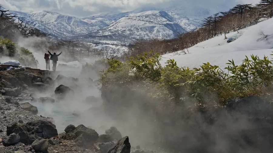 Tourists admire the steam of the picturesque thermal spring (Boiling River) near the Baranovsky volcano, the water temperature in the source of which is 80 degrees.