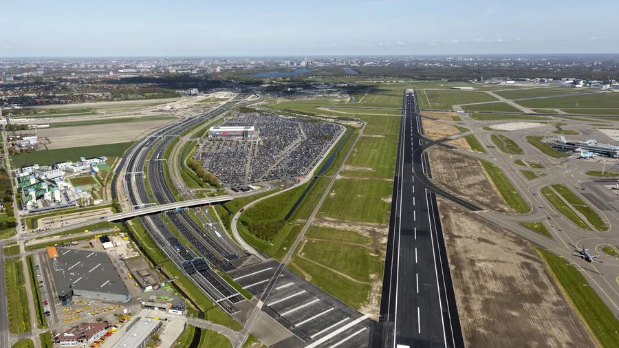 Aerial view of expansive international airport with runways, highways, parking lots, and terminals showcasing complex infrastructure.