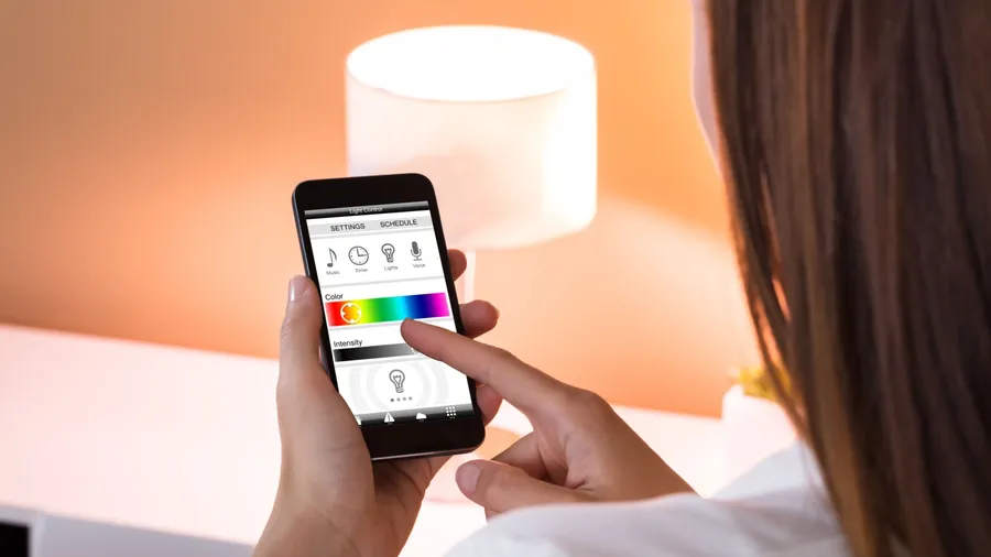 A woman using her smartphone to adjust the light of a smart lamp.