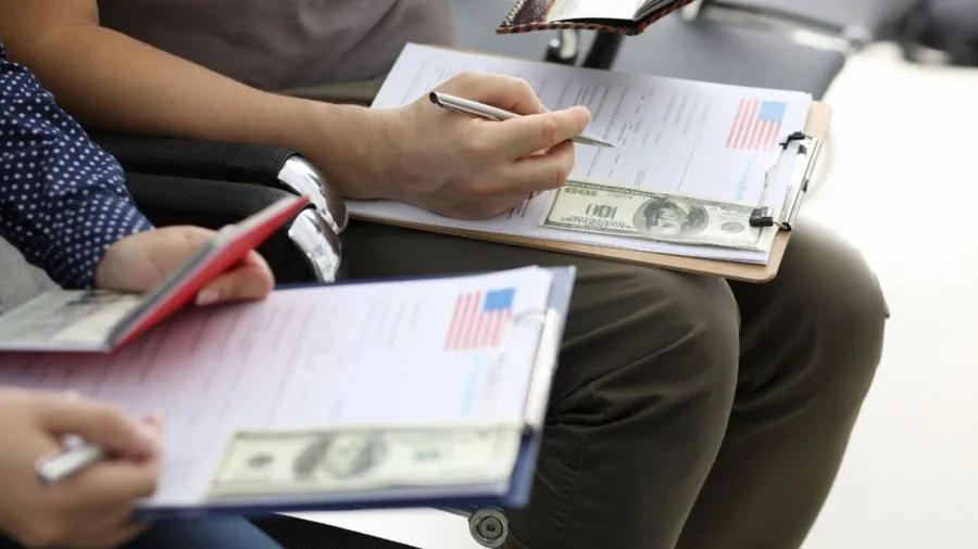 Close-up view of people filling usa visa application forms with personal passports at embassy.