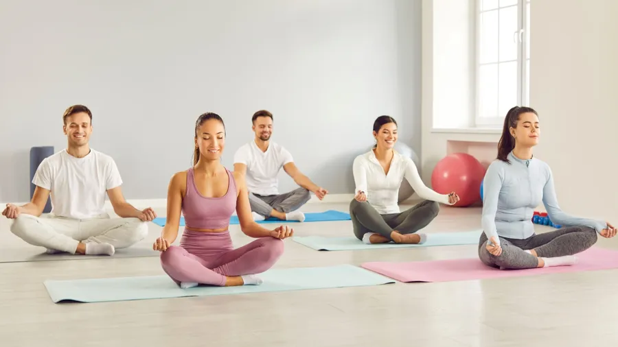 Positive people group in yoga meditation session at sport gym. Sitting in the serene lotus position, happy team relaxing at yoga class, practicing zen, improves mental health.