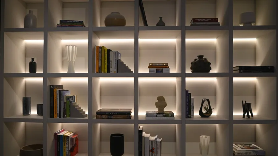 A white backlit bookshelf with books, bookends, and sculptural decor accents.