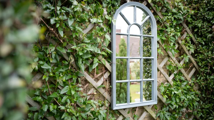 A decorative mirror surrounded by lush green ivy on a lattice wall.